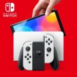 Console Nintendo Switch OLED modèle blanc avec écran allumé montrant un paysage coloré.